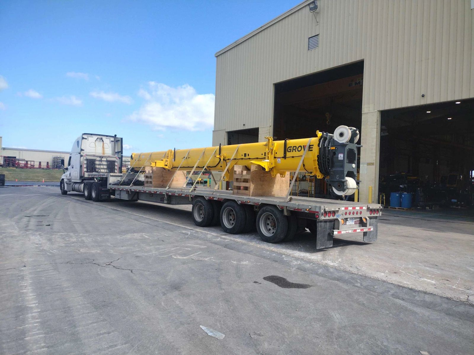 An open-deck trailer carrying industrial equipment beside a loading facility